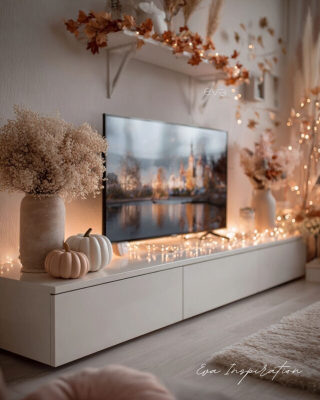 Banc TV décoré pour l’automne avec citrouilles blanches, fleurs séchées et guirlandes lumineuses.