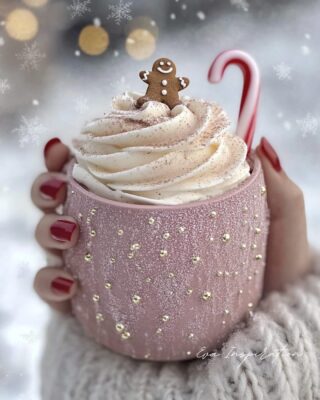 Chocolat chaud dans une tasse rose poudré décorée de perles dorées, avec crème, sucre d’orge et bonhomme pain d’épices, neige et manucure rouge
