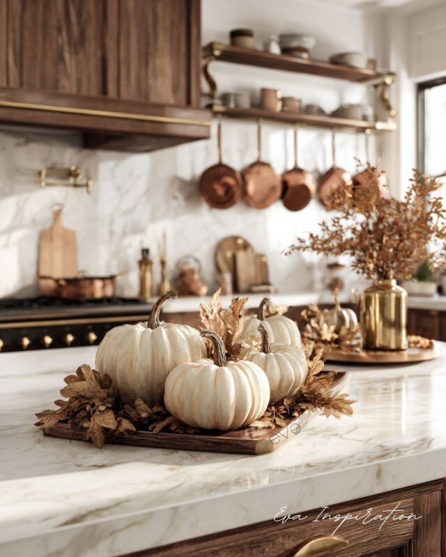 Décoration automne maison : citrouilles blanches sur îlot de cuisine en marbre, détails cuivre et feuilles séchées