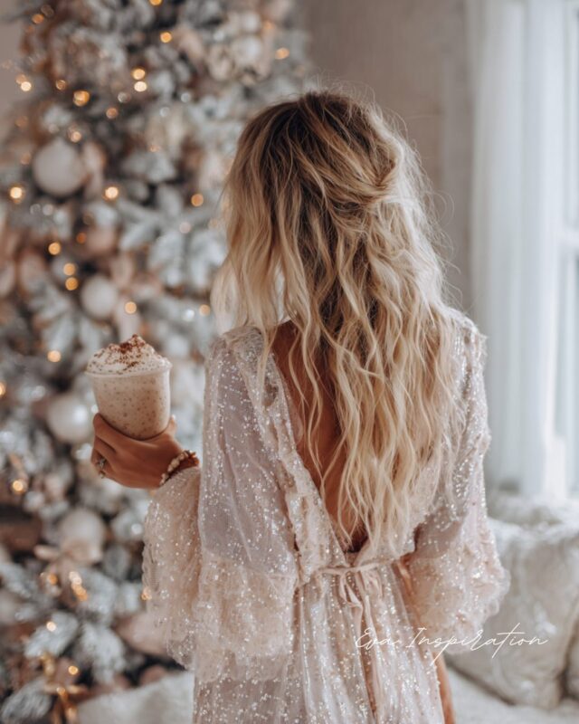 Boisson froide de Noël à la cannelle, tenue par une femme en robe pailletée devant un sapin blanc décoré